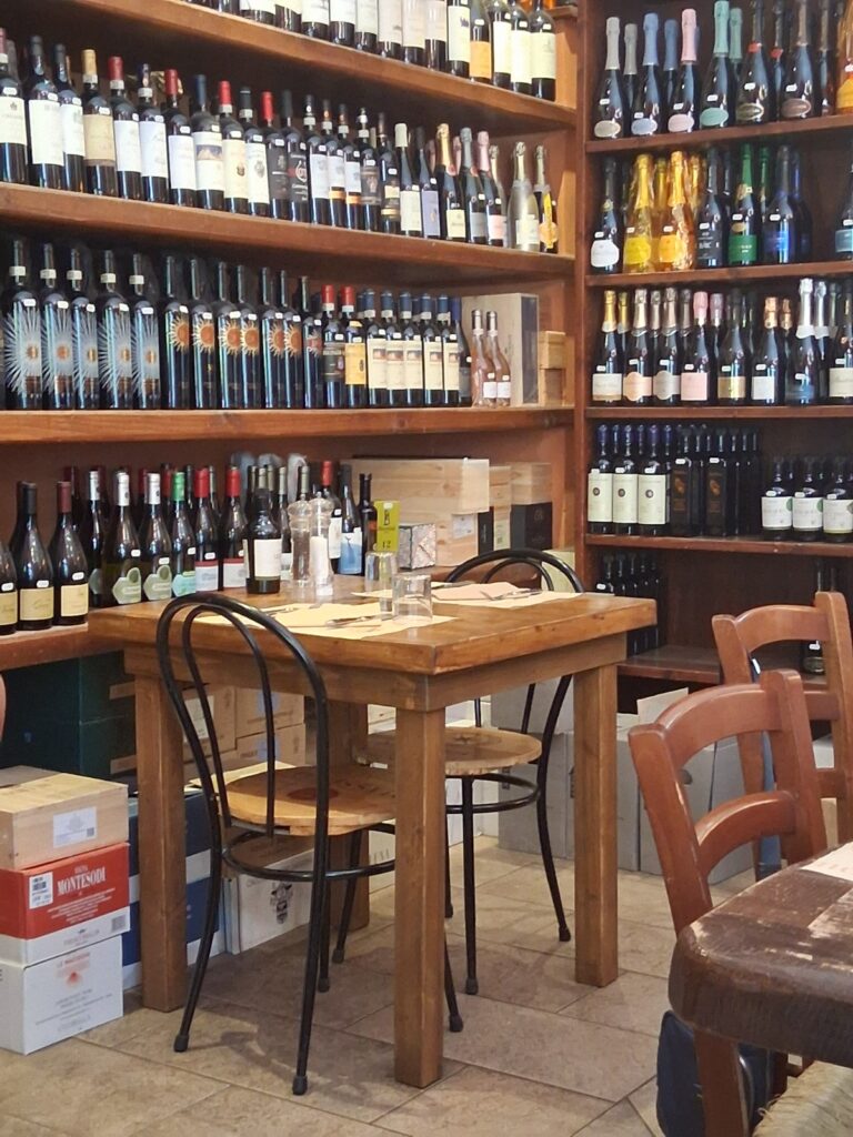 Wine shop interior with wooden shelves packed with bottles and a central wooden table for tasting or service.