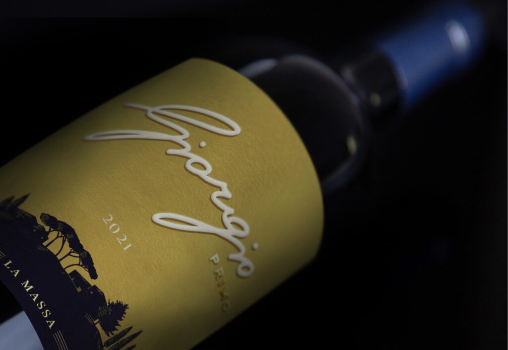 Close-up of a yellow wine bottle label with white cursive text and a black landscape illustration on the bottom edge.