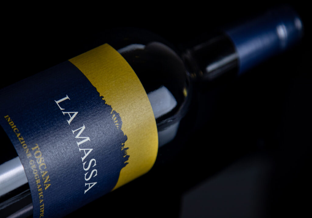Close-up of a wine bottle on its side with a blue and gold La Massa label visible in focus.