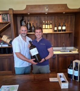 Mark's Meanderings and Clemente Zileri del Verme behind a wooden wine bar, smiling as they hold a large bottle of wine together in Castello di Bolgheri tasting room.
