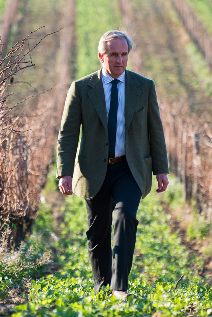 Federico Zileri Dal Verne in a green blazer and blue tie walking along a vineyard row outdoors.