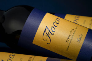 Diagonal shot of a wine bottle with blue and gold label; text includes Italia and Toscana.